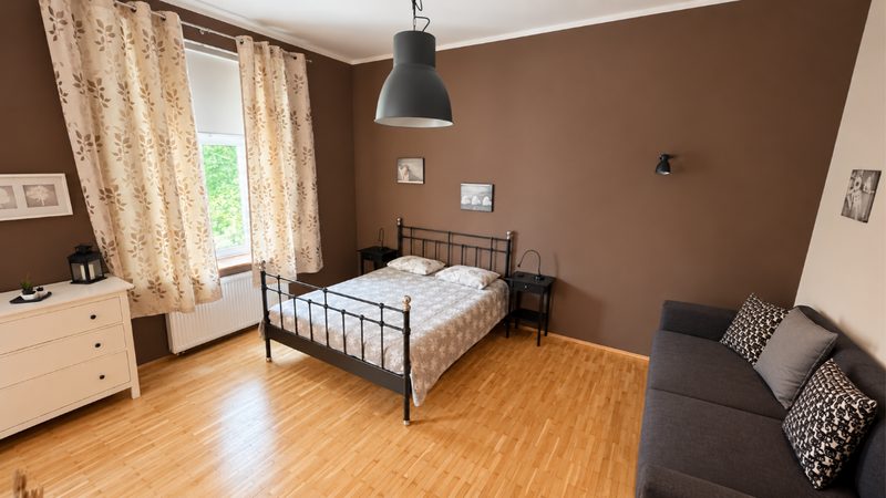 Bright bedroom at ELPIDA Kraków with double bed, sofa and tall curtained window